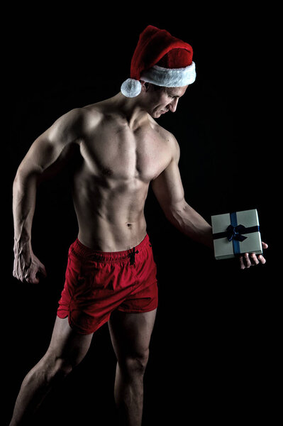 Красивая концепция Санты. Мускулистое туловище с подарочной коробкой. Санта Клаус для взрослых девочек. Сексуальная спортивная мускулистая грудь в шляпе Санта Клауса. Спортсмен носит шляпу Санты. У меня для тебя подарок.
