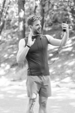 Seni gördüğüme çok sevindim. Çalıştırmadan önce atlet cep telefonu video seslenmek. Adam atlet gülümseyen yüz çevrimiçi eğitim koç, Doğa arka plan bakın. Adım sayar ve kulaklık ile sporcu online video eğitim