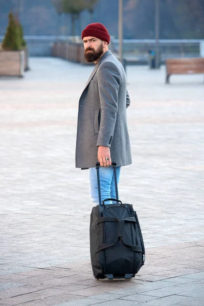 Traveler with suitcase arrive airport railway station urban background. Hipster ready enjoy travel. Carry travel bag. Man bearded hipster travel with luggage bag on wheels. Adjust living in new city
