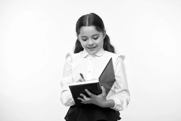 Uczennica pisze w notatniku na żółtym tle. Dziewczyna w szkolnym mundurze, z powrotem do szkoły. Małe dziecko z notatnikiem. Geniusz mody. Tworzenie mojej przyszłości — Zdjęcie stockowe