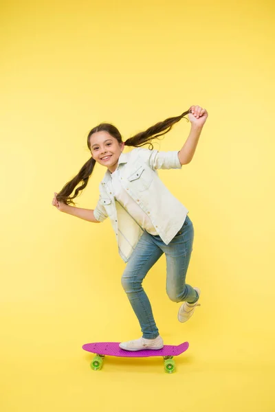 趣味好きな活動。子供の笑顔の顔はスケートボードに立つ。ペニーボード女の子のためのかわいいカラフルなスケートボード。乗るぞ。女の子に乗るペニーボード黄色の背景。子供持って楽しいですペニーボード — ストック写真