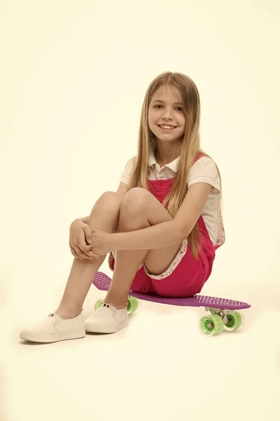 Mała dziewczynka siedzieć na pokładzie skate na białym tle. Dziecko uśmiech skater z longboard. Deskorolka dziecko w różowy kombinezon. Aktywność sportowa i energii. Dzieciństwo i aktywnej gry. Piękno na deskorolce. — Zdjęcie stockowe