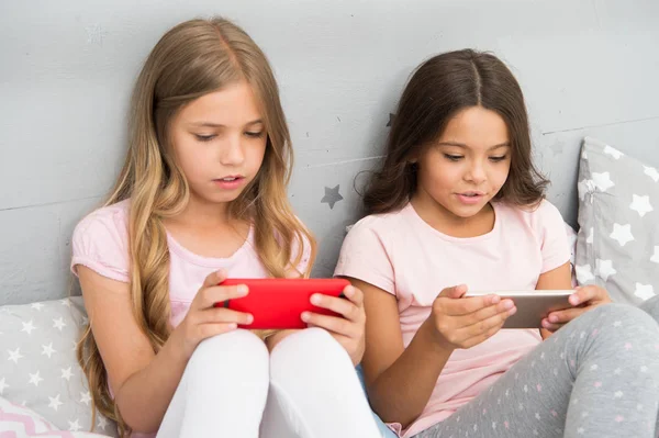 Kinderen in pyjama communiceren met smartphones. Aanvraag voor kinderen plezier. Internet surfen en afwezigheid ouderlijk advies. Smartphone internettoegang. Meisjes zusters dragen pyjama bezig met smartphones — Stockfoto