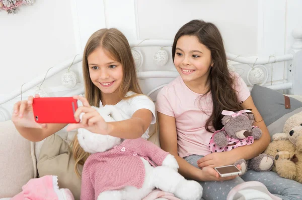 Living in the moment. Merry Christmas and Happy New Year greetings. Taking Christmas and New Year selfie with smartphone. Little girls use phone in bed. Happy little children with mobile phone