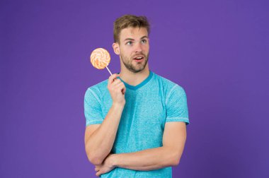 Yemek kavram hile. Şeker sağlık için zararlı. Adam lolipop şeker menekşe arka plan tutun. Adam yakışıklı maço büyük renkli tatlı lolipop yemek. Çocukluk tadına. Kıl adamla Lolipop sever