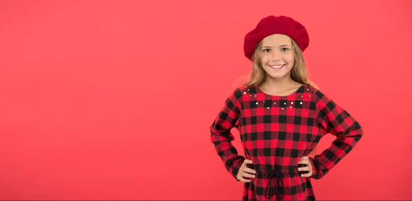 Draag baret als mode meisje. Kid beetje schattig meisje met lang blond haar poseren in baret hoed en geruite jurk rode achtergrond. Baret stijl inspiratie. Modieuze baret accessoire voor vrouwelijke — Stockfoto