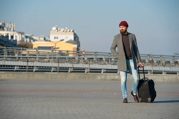 Hipster ready enjoy travel. Carry travel bag. Man bearded hipster travel with luggage bag on wheels. Traveler with suitcase arrive airport railway station urban background. Moving to new city alone