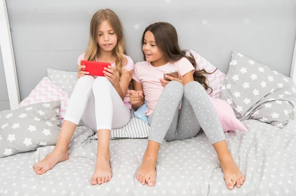 Αδερφές κορίτσια φορούν pajama απασχολημένος με smartphones. Παιδιά pajama αλληλεπιδρούν με τα smartphones. Αίτηση για τα παιδιά διασκεδάζουν. Σερφάρισμα στο διαδίκτυο και απουσία συμβουλευτική γονέων. Πρόσβαση στο internet smartphone — Φωτογραφία Αρχείου