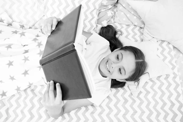 Girl child lay bed read book top view. Encourage useful habits.Kid prepare to go to bed. Pleasant time in cozy bedroom. Girl kid long hair cute pajamas relax and read book. Satisfied with happy end