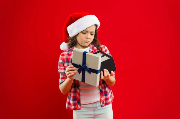 Felices fiestas de invierno. Pequeña chica seria. Regalo para Navidad. Infancia. Compras de Navidad. Niña con sombrero rojo de santa. Fiesta de año nuevo. Chico Santa Claus. Gran regalo —  Fotos de Stock