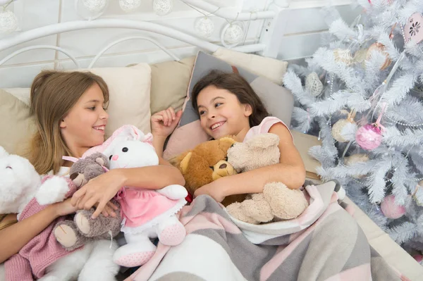 They love Christmas. Little children enjoy Christmas. Little children have Christmas fun. Small girls play with toys. Happy kids in bed at Christmas tree. Childhood games on xmas and new year — Stock Photo, Image