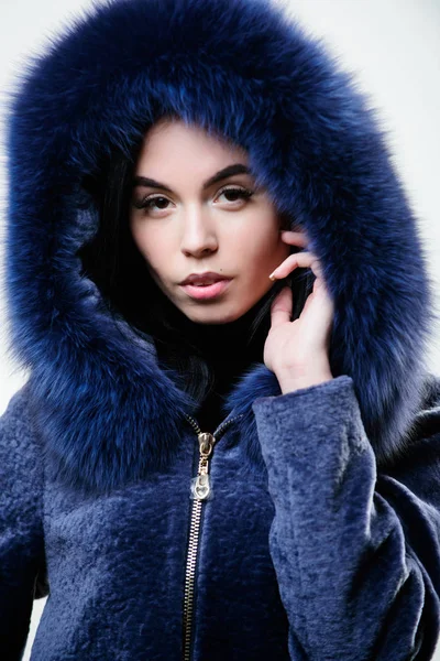 Female with makeup wear dark blue soft fur coat. Woman wear hood with fur. Fashion concept. Girl elegant lady wear fashionable coat jacket with furry hood. Luxurious fur. Girl posing hooded fur coat