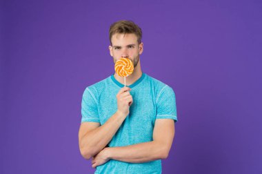 Kıl adamla Lolipop sever. Yemek kavram hile. Şeker sağlık için zararlı. Adam lolipop şeker menekşe arka plan tutun. Adam yakışıklı maço büyük renkli tatlı lolipop yemek. Çocukluk tadına