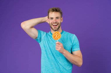 Adam yakışıklı maço büyük renkli tatlı lolipop yemek. Çocukluk tadına. Sakallı adam Lolipop sever. Tatlıya kavramı. Şeker sağlık için zararlı. Adam tutun lolipop şeker menekşe arka plan