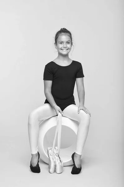 子供の柔軟な体操のストレッチの先端。子供の柔らかいダンサーは豪華な空想のレオタードに見えます。すべての女の子は有名な体操になる夢。子供はポイントバレエシューズを保持座っている。バレエのための特別な靴 — ストック写真