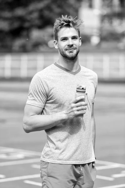 アスレチック外観を持つ男は、水のボトルを保持します。選手は、晴れた日にスタジアムでトレーニング後、水を飲みます。スポーツと健康的なライフ スタイルのコンセプト。屋外トレーニング スポーティな服で男選手 — ストック写真