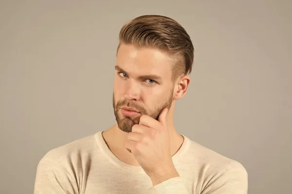 Bearded man touch beard with hand. Macho with stylish hair and healthy young skin. Guy with unshaven face and mustache. Beard grooming and hair care in barbershop. Skincare and mens beauty concept