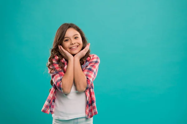 Niño feliz cara linda con adorable pelo rizado de pie sobre fondo azul. Pura belleza. Consejos de belleza para el cabello ordenado. Niña larga y saludable pelo brillante llevar ropa casual. Niña con el pelo largo —  Fotos de Stock