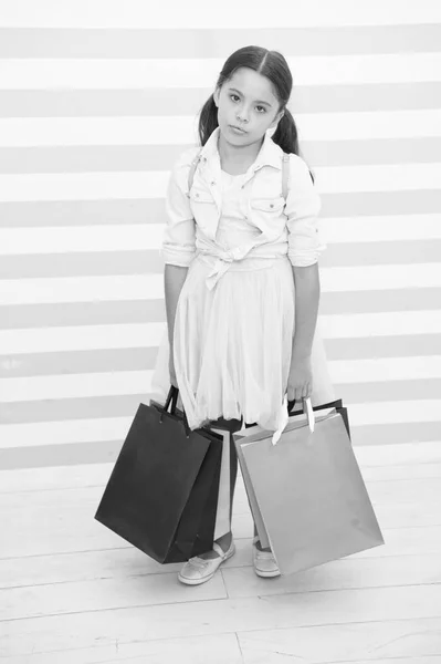 Compras agotadoras actividad agotadora. Niño lleva bolsas de compras fondo rayado. La niña pasa el día comprando cosas para la escuela. De vuelta a la temporada de ventas escolares. Chica agotado sostiene bolsas —  Fotos de Stock