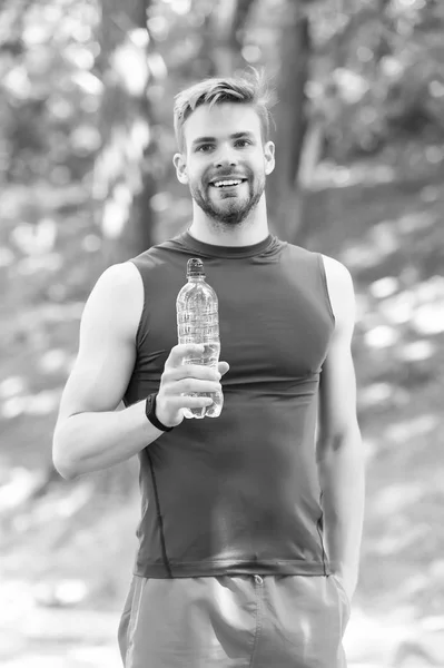Спортсмен п'є воду після тренування в парку в сонячний день. Чоловік атлетично привабливий зовнішній вигляд тримає пляшку води. Чоловік спортсмен спортивного одягу тренується на відкритому повітрі. Спорт і концепція здорового способу життя — стокове фото