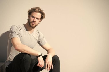 Sakallı ve günlük tişörtlü sarı saçlı adam. Maço açık havada akıllı telefon tutar. Gri duvarda cep telefonu olan sakallı bir adam. Yeni teknoloji ve modern hayat, boşluğu kopyala