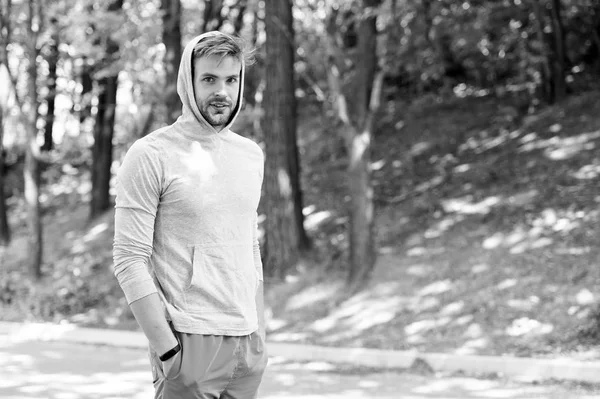 Taking minute break. Runner workout outdoor. Man athlete with hood after running outdoor, nature background. Athletic man relaxing break. Athlete hooded takes break during exhausting training