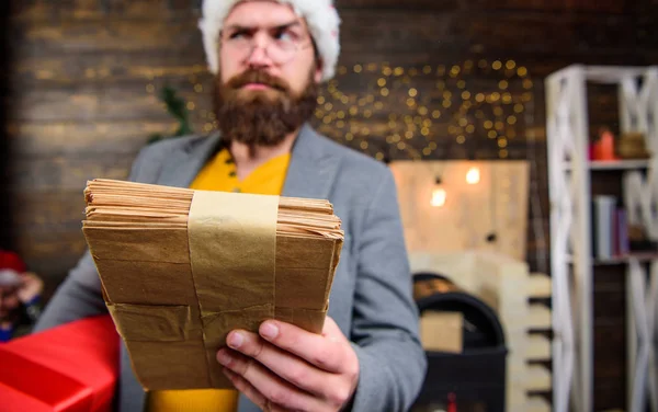 Man bearded hipster wear santa hat hold bunch of letters and gift box. Letter for santa claus. Man mature bearded with eyeglasses received post for santa. Gifts delivery service. Post for santa claus