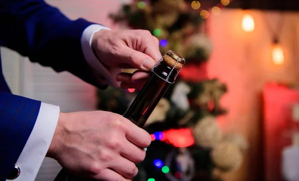 Lets celebrate. Open champagne and celebrate holiday. Celebrate new year with champagne drink. Toast and cheers concept. Male hands opening champagne bottle on christmas decorations background
