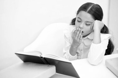 Boring literature. Girl child reads book while sit table white background. Schoolgirl studying and reading book. Kid girl school uniform bored yawning face sadly read boring literature. Tiresome task clipart