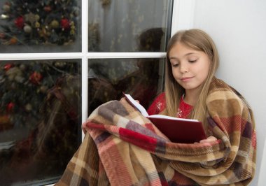 Çocuk kitabı. Küçük çocuk Noel arifesinde kitabını okudum. Küçük kız Noel hikaye okuma keyfini çıkarın. Küçük okuyucu üzerinde pencere pervazına ekose Sit. Sihirli Noel ruhu. En iyi Noel kitap