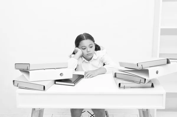学得太多了。小女孩累得筋疲力尽坐在桌旁的一堆白纸背景。女生厌倦了读书和看书。孩子学校制服疲倦的面孔不想继续读书 — 图库照片
