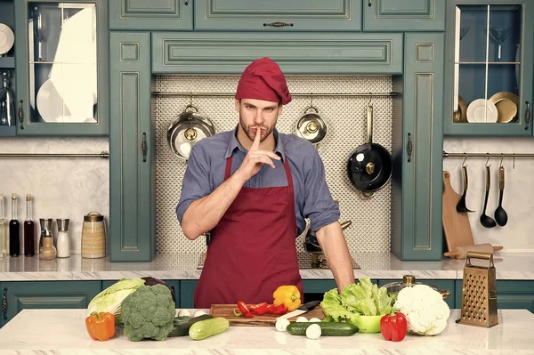 Chef-kok met stilte gebaar vinger aan tafel met groenten. Cook geheime schotel van de man in de keuken. Ingrediënten voor het koken veganistisch eten. Vegetarisch menu en gezonde voeding. Voedselbereiding en koken van recepten — Stockfoto