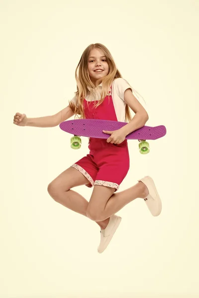 Find your freedom Small girl jump with skate board isolated on white. Child skater smile with longboard. Skateboard kid in pink jumpsuit. Sport activity and energy. Childhood and active games