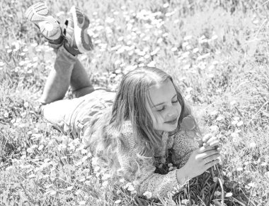 Bahar tatili kavramı. Çocuk zevk çayır papatya çiçekleri ile yatarken bahar güneşli gün. Yüz gülümseyerek kıza kırmızı lale çiçek tutan, aroma burnunu çekmek. Çimen, grassplot arka plan üzerinde yatan kız