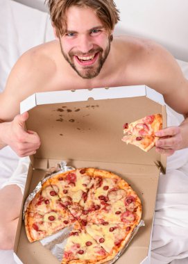 İç çamaşırı aç genç adam evde pizza kutusu ile bir yatakta oturur. Diyet hakkında kimin umurunda. Gömleksiz seksi adam yatakta pizza ile görüntü kırpılmış. Yatakta yemek.