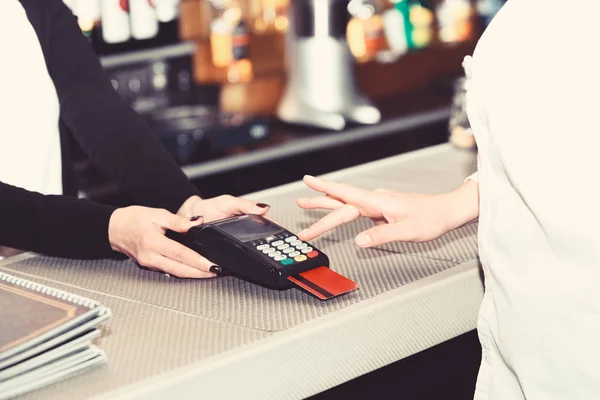 Caixa mão detém terminal de cartão de crédito em fundo desfocado — Fotografia de Stock