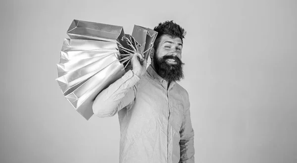 Hipster op knipogend gezicht winkelen. Guy winkelen op verkoop seizoen, draagt stelletje zakken op de schouder. Man met baard en snor houdt boodschappentassen, grijze achtergrond. Winkelen op concept — Stockfoto