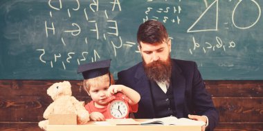 Sıkılmış çocuk saati ile oynamak. Bireysel eğitim kavramı. Öğretmen formal giyim ve öğrenci sınıfta kolej, kara tahta arka plan. Öğretmen, ödev, kontrol baba küçük oğlu için yardımcı olur.