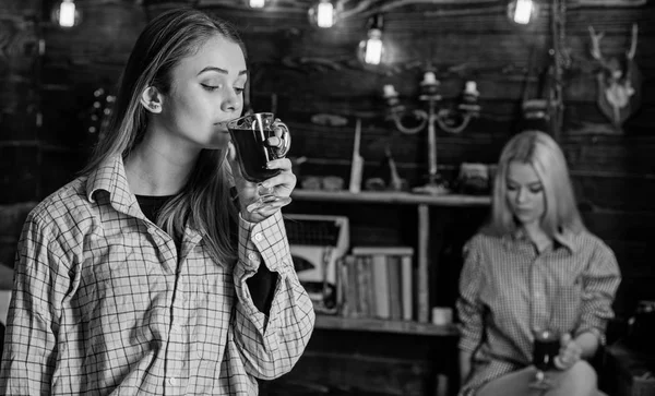 Friends enjoy mulled wine in warm atmosphere, wooden interior. Girls relaxing and drinking mulled wine. Rest and relax concept. Friends on relaxed faces in plaid clothes relaxing, defocused — Stock Photo, Image