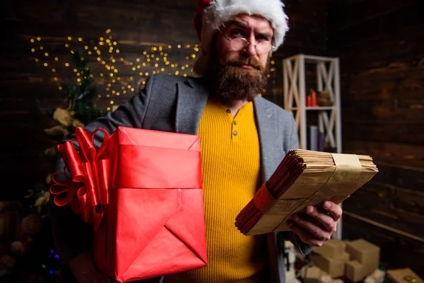 Man bearded hipster wear santa hat hold bunch of letters and gift box. Man mature bearded with eyeglasses received post for santa. Gifts delivery service. Letter for santa claus. Post for santa claus