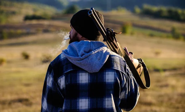 Hunter carry rifle gun on shoulder rear view. Guy hunter spend leisure hunting. Hunting masculine hobby leisure concept. Man brutal guy gamekeeper in hat nature background. Brutality and masculinity