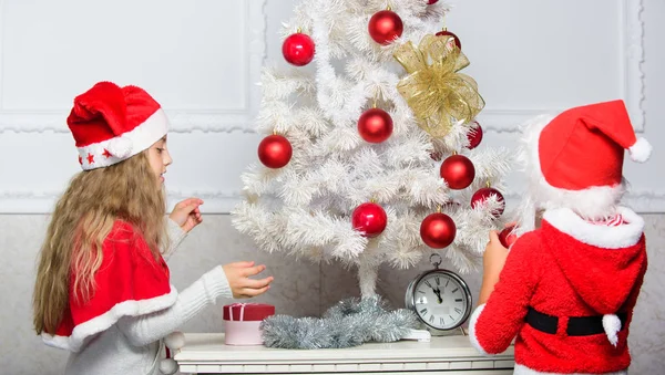 Children decorating christmas tree together. Siblings busy decorating. Boy and girl decorating tree. Cherished holiday activity. Kids in santa hats decorating christmas tree. Family tradition concept