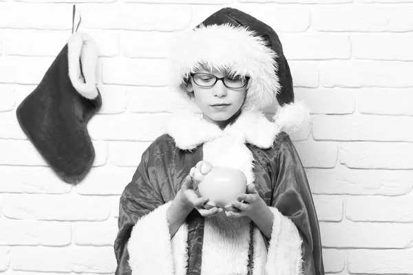 귀여운 산타 클로스 소년 장식 크리스마스 나 크리스마스 스타킹 이나 부팅 지주 핑크 돼지 돼지 은행 흰색 벽돌 벽 바탕에 빨간색 스웨터와 새 해 모자에 안경 — 스톡 사진