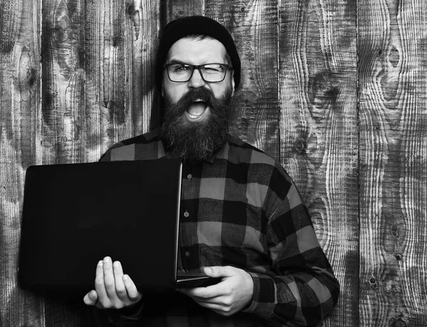 Sakallı adam, uzun sakal. Acımasız beyaz tıraşsız hipster dizüstü şapka ve gözlük kahverengi vintage ahşap studio adam kırmızı siyah damalı gömlek holding — Stok fotoğraf