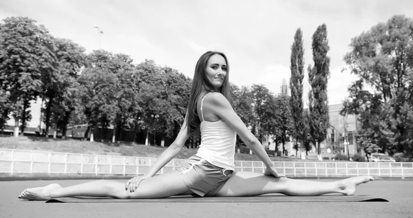 Γυναίκα εύκαμπτα body πρακτική split σε γυμναστήριο χαλί σε εξωτερικούς χώρους φύση φόντο. Κορίτσι που εκτείνεται στα πόδια μετά την προπόνηση. Split είναι εύκολο έργο. Τέντωμα των μυών κάθε φορά κατάρτισης. Προπονητής συμβουλές και συμβουλές — Φωτογραφία Αρχείου