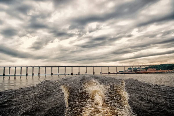 Rastros de lancha rápida en el agua azul del mar en Manaus, Brasil. Paisaje marino con puente en el horizonte en el cielo nublado. viajes y vacaciones. concepto de arquitectura y diseño — Foto de Stock