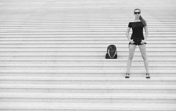 Menina turista stand escadas pedregosas perto de sua mochila. Pronto para explorar nova cidade. Mulher óculos de sol elegante roupa preta andando Paris. Conceito de férias e viagens. Guia turístico excursão turística — Fotografia de Stock