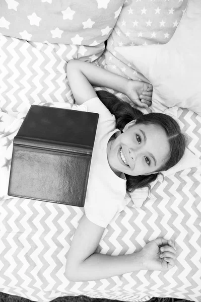 Дівчинка з ліжком читає книгу зверху. Малюк готується йти спати. Приємний час у затишній спальні. Дівчинка довге волосся мила піжама розслабляється і читає книгу. Заохочувати корисні звички. Задоволений щасливим кінцем — стокове фото