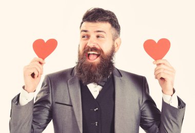 Hipster resmi takım elbise giyiyor. Uzun sakallı ve güler yüz ile mutlu bir adam. Sakallı adam gülümsüyor ve kırmızı kalpler tutar. Dating, aşk, romantizm, sembol, moda, stil, duygular, duygular, flört kavramı