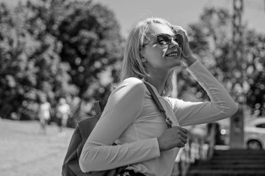 Kadın güneş gözlüğü yürüyüş güneşli bir gün, kentsel arka plan tadını çıkarın. urious turist. Trendy kız yürüyor. Açık havada duran süre sırt çantası taşıyan bir kadın. Şık sırt çantası ile kız yürüyor